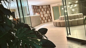 A modern interior with a glass partition, a plush sofa, a bookshelf, and large green plants. - Hotel Casa Victoria Medellín (Medellín)