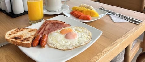 A breakfast plate with toast, sausages, a fried egg, and a glass of orange juice.