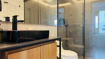Un baño moderno con ducha de vidrio, lavamanos negro y retrete blanco.