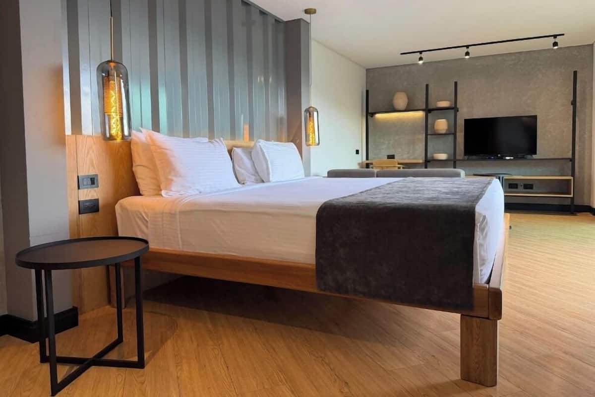 A modern hotel room with a wooden bed, a round table, a TV, and a wall-mounted shelf.