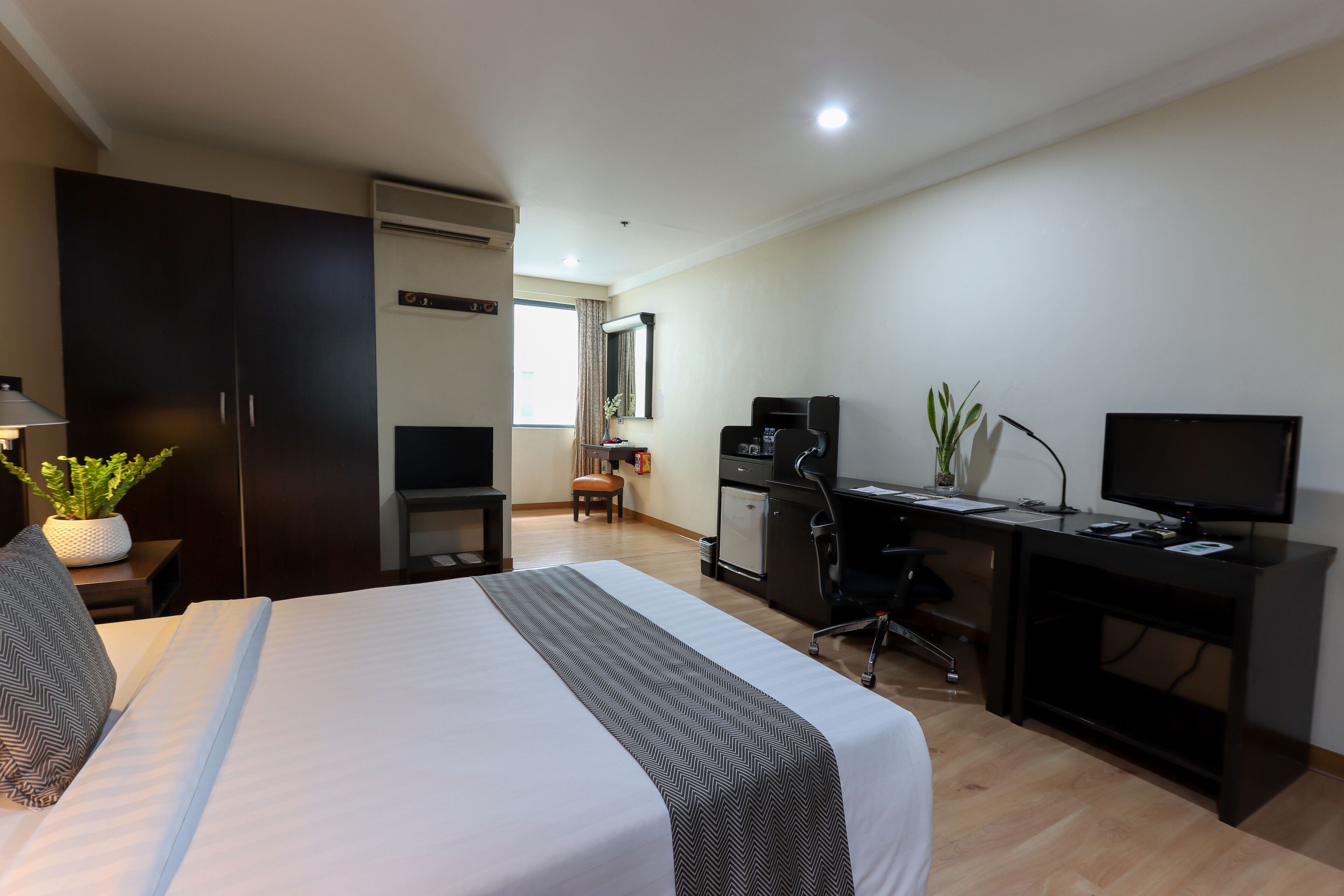 A hotel room with a bed, a desk, a television, and a small kitchenette.