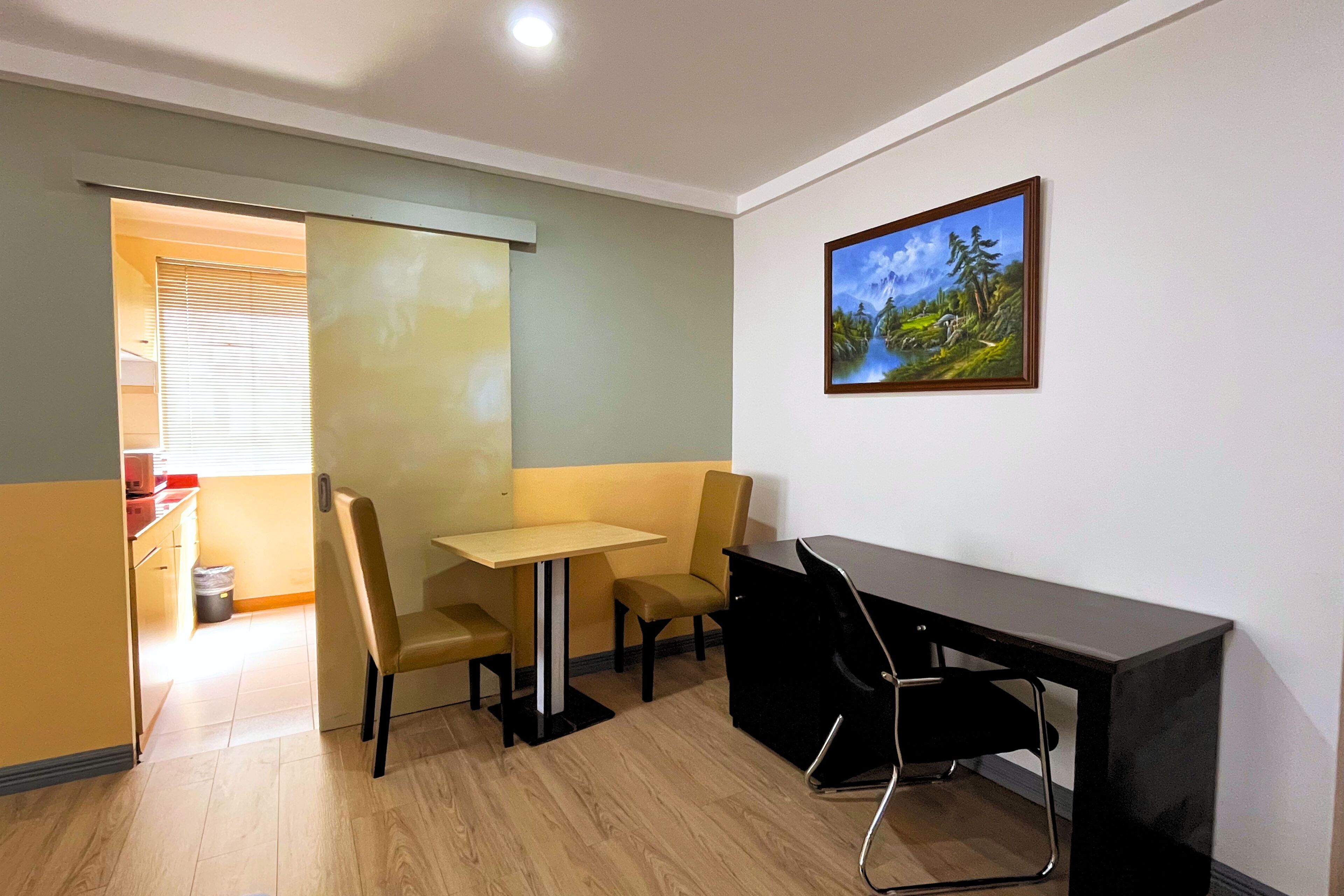 A small office with a desk, two chairs, a table, and a painting on the wall.