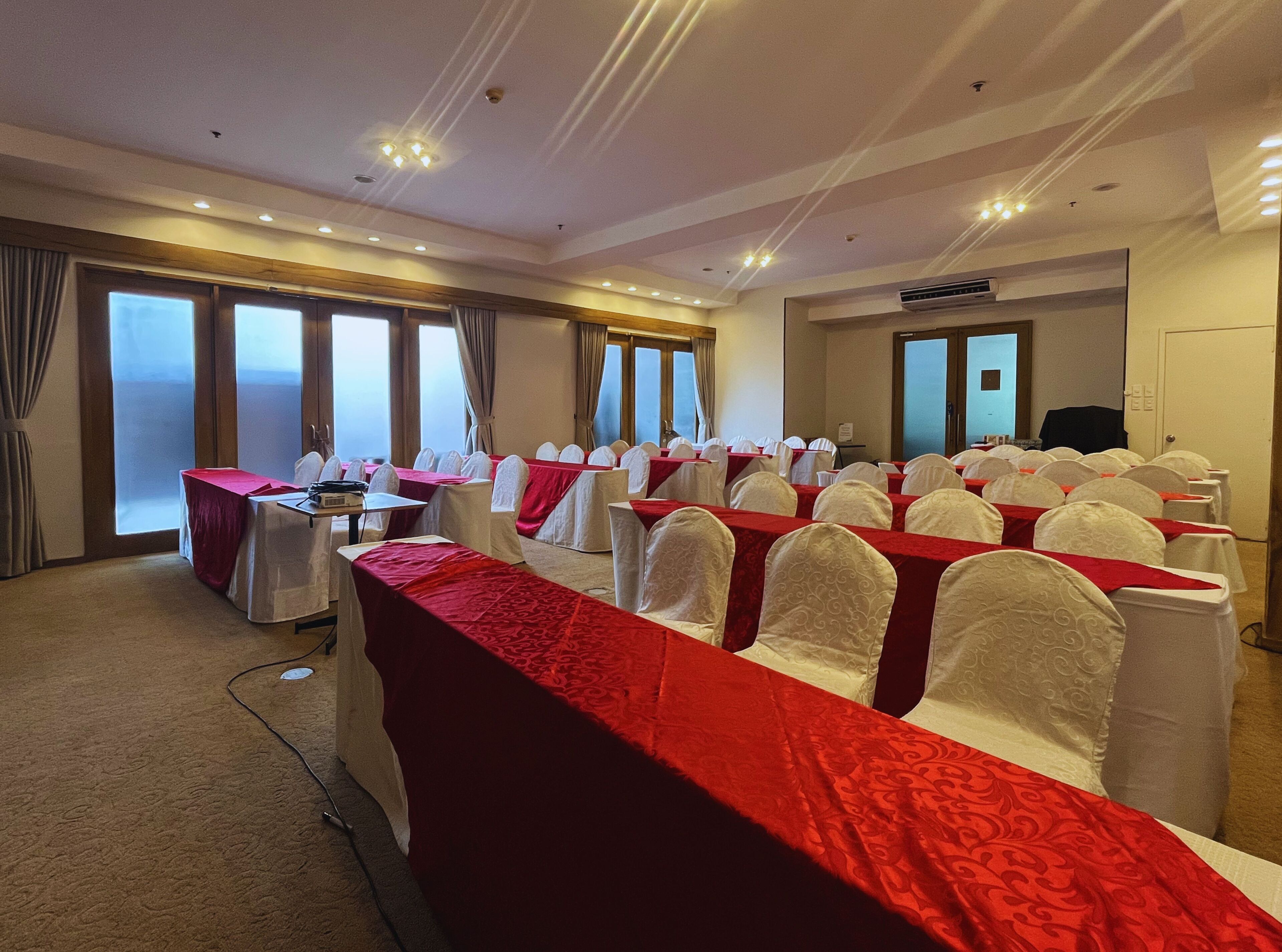 Un salón de conferencias con filas de mesas, sillas blancas y manteles rojos.