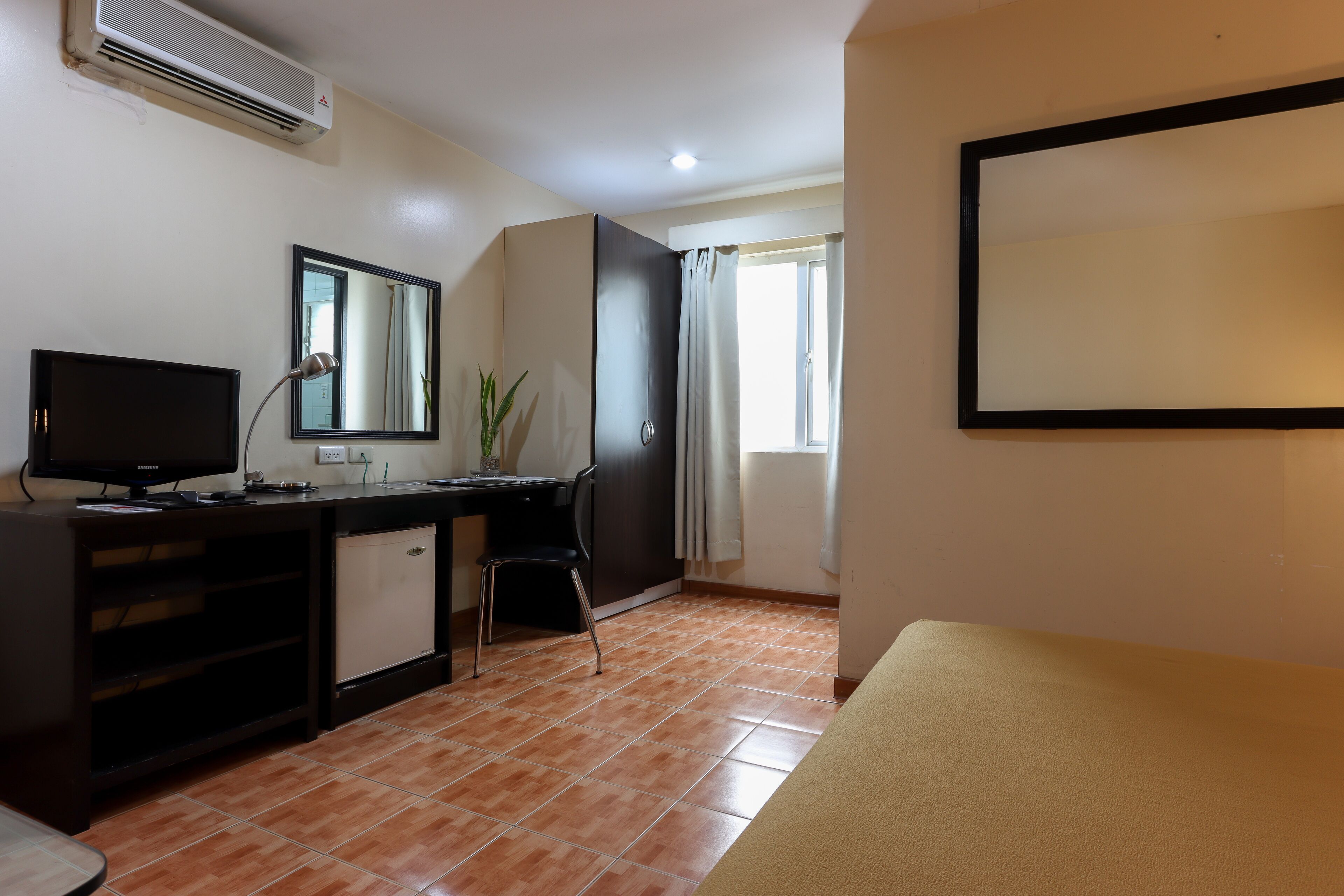 A room with a desk, chair, television, air conditioning unit, and a bed.