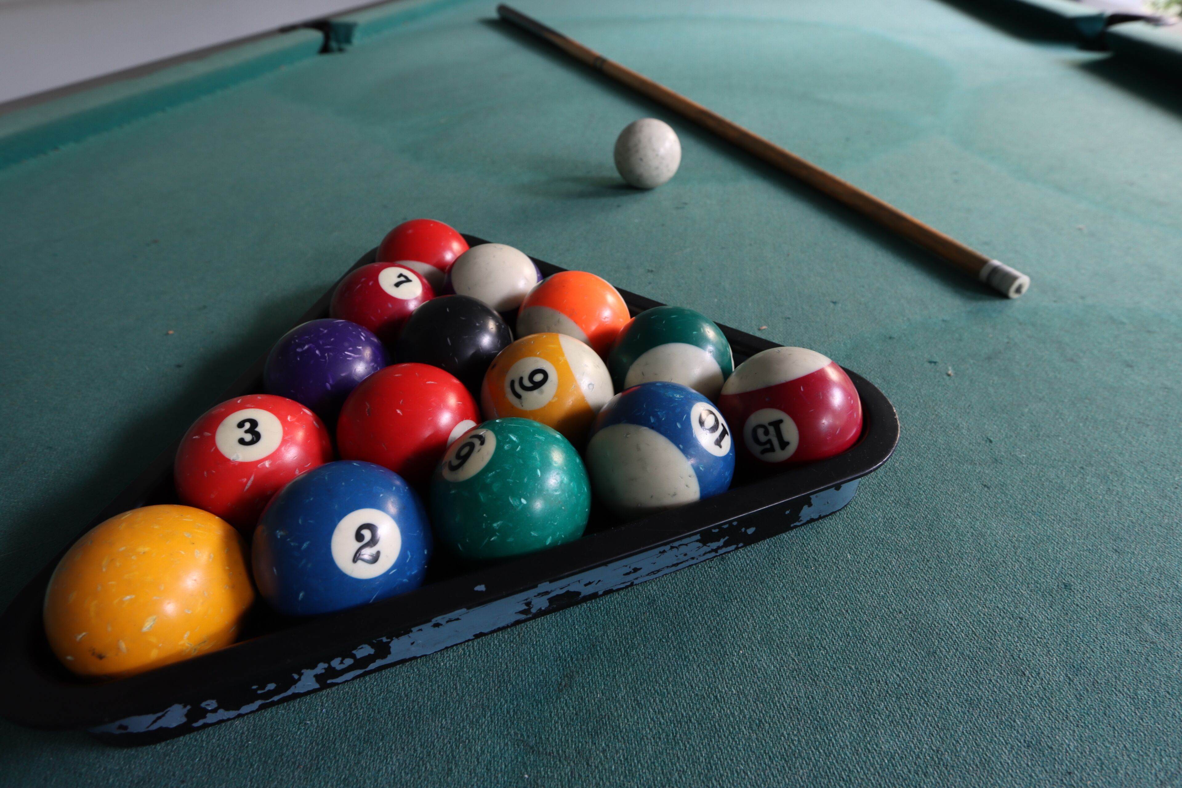 A pool table with a set of numbered billiard balls and a cue stick.