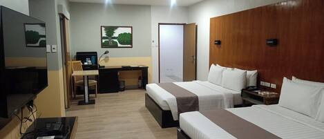 A hotel room with two beds, a desk, a chair, a TV, and a small table with electronic devices.