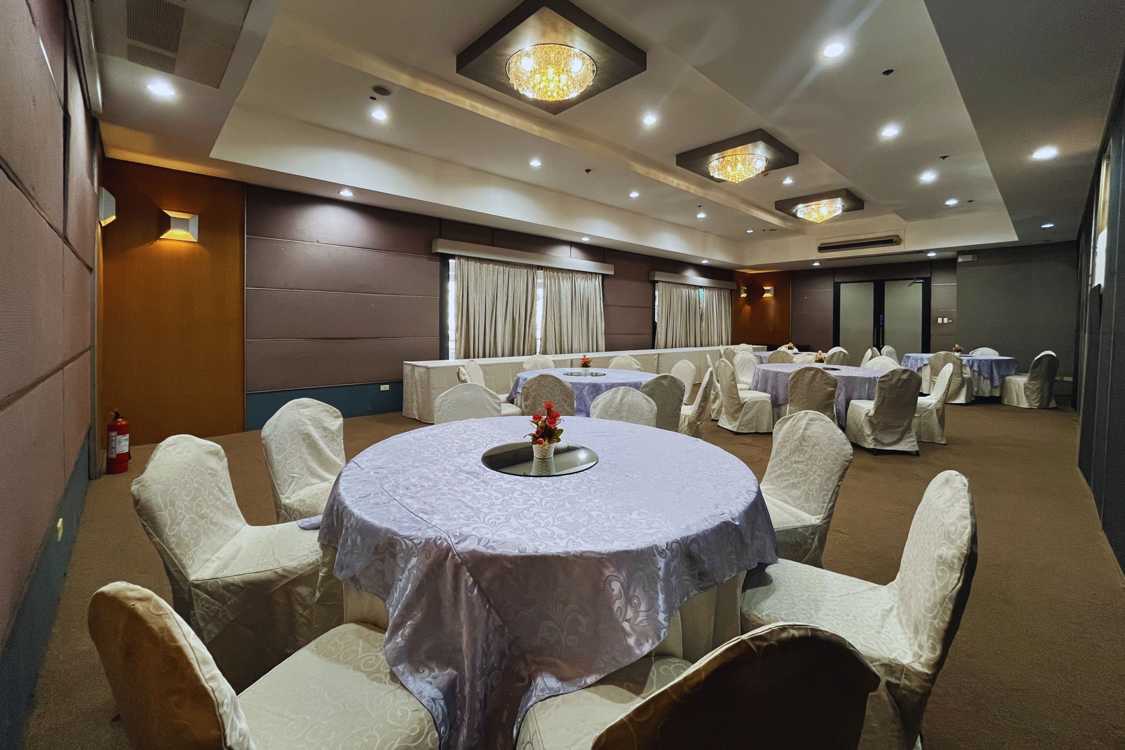 A banquet hall with round tables, chairs, and chandeliers.