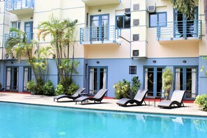 A hotel with a swimming pool, lounge chairs, and balconies with railings.