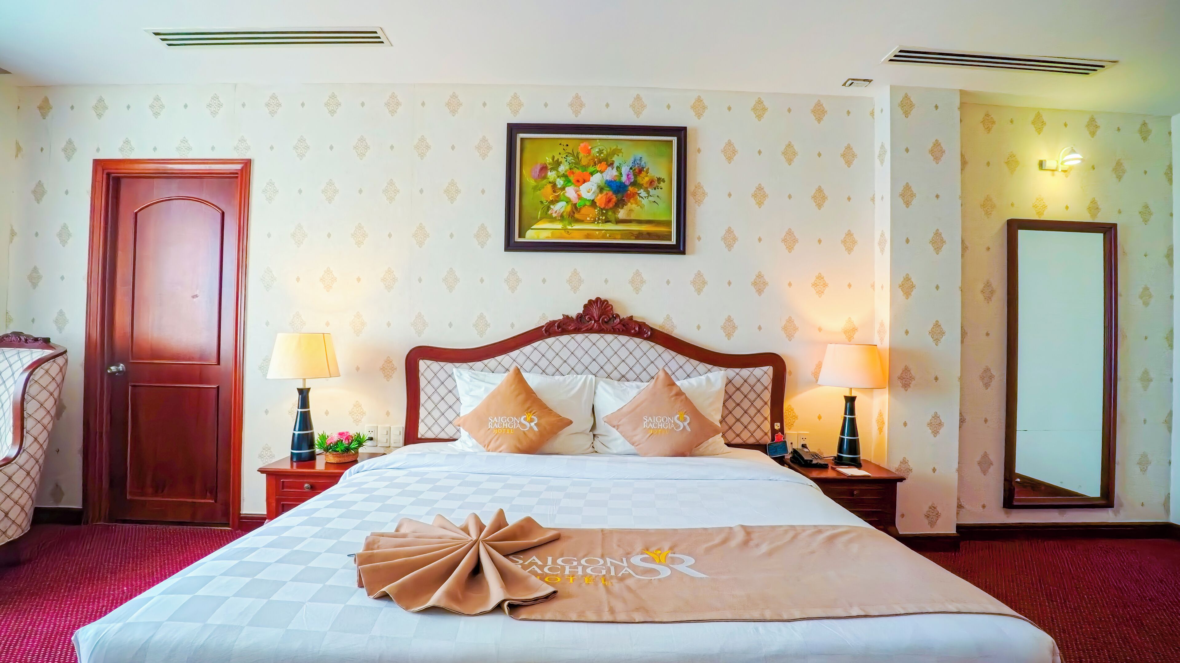 Een hotelkamer met een bed, twee nachtkastjes, een spiegel, een deur en een muur met een bloemschilderij.
