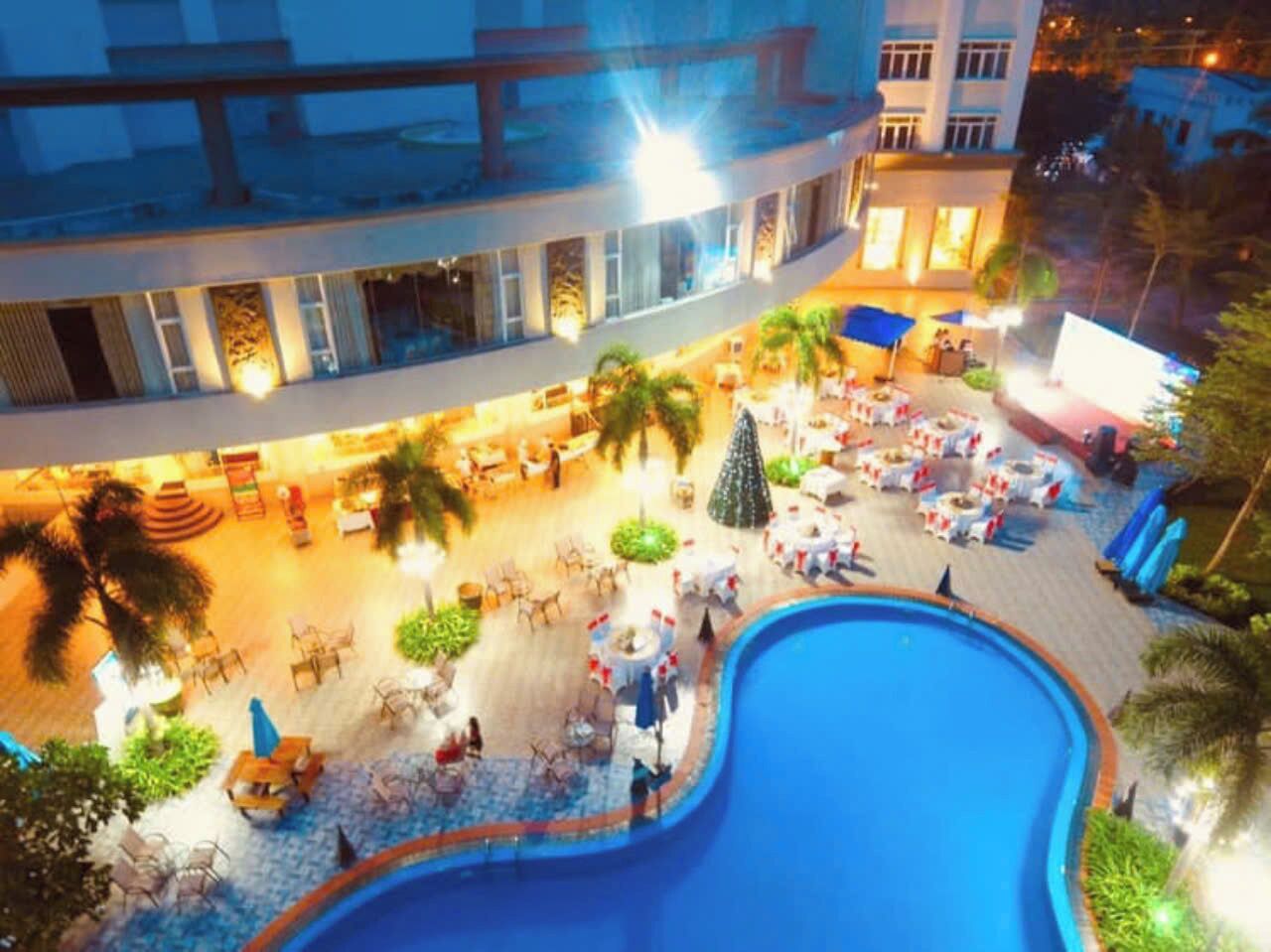 A hotel pool area with outdoor seating, palm trees, and a large pool.