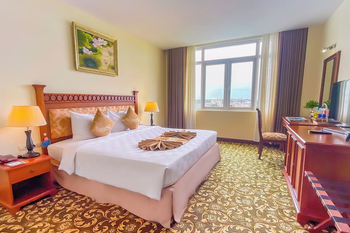 A hotel room with a large bed, two bedside lamps, a desk with a TV, and a window with curtains.
