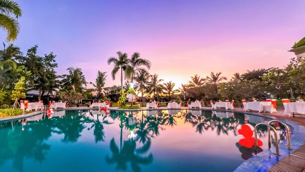 A pool area with tables and chairs, surrounded by palm trees and a sunset sky. - Sai Gon Rach Gia Hotel (Rach Gia)