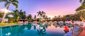 A pool area with tables and chairs, surrounded by palm trees and a sunset sky. - Sai Gon Rach Gia Hotel (Rach Gia)