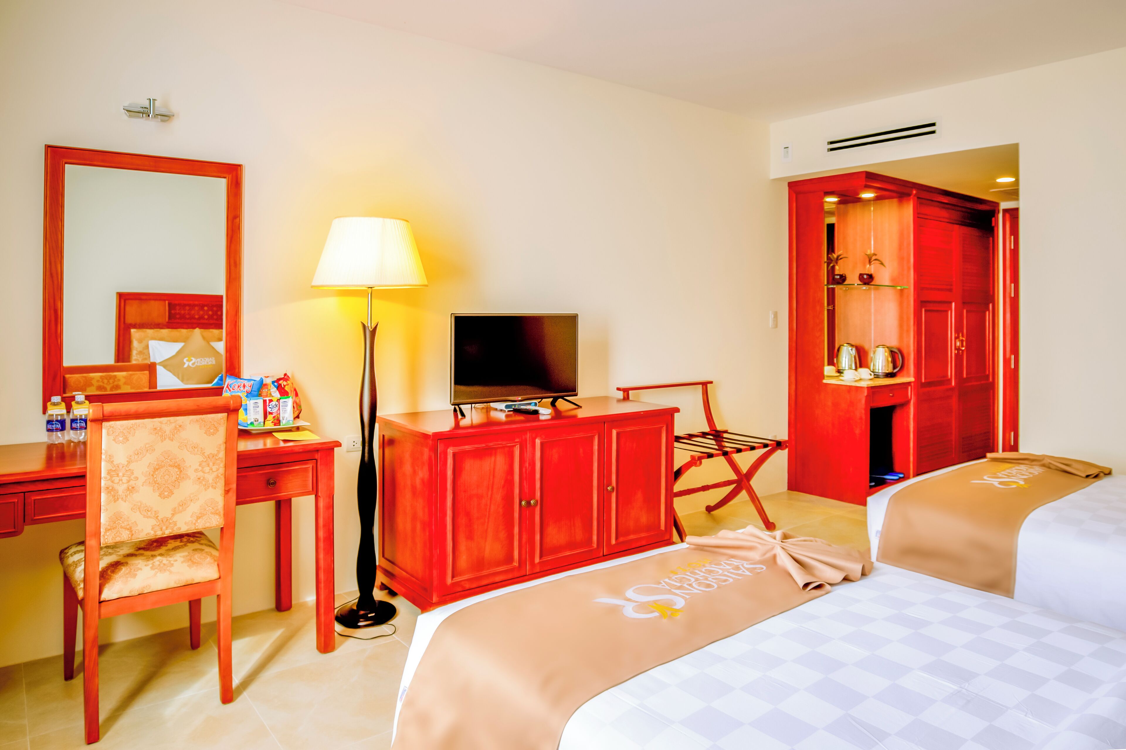 A hotel room with a desk, chair, television, wardrobe, and two beds.
