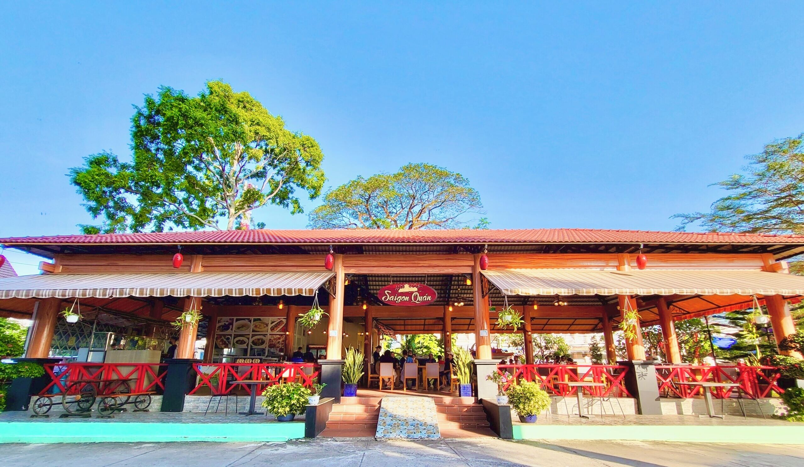 A restaurant with a red roof and wooden structure, outdoor seating, and potted plants.