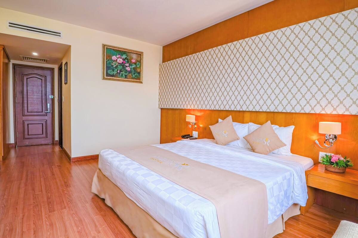A hotel room with a large bed, two bedside tables, a headboard with a patterned design, a door, and a framed picture on the wall.