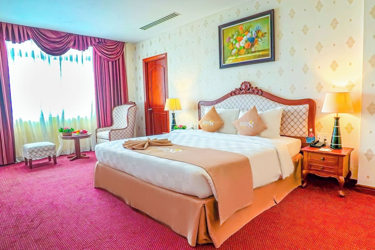A hotel room with a large bed, a chair, a bedside table with a lamp, and a painting on the wall.