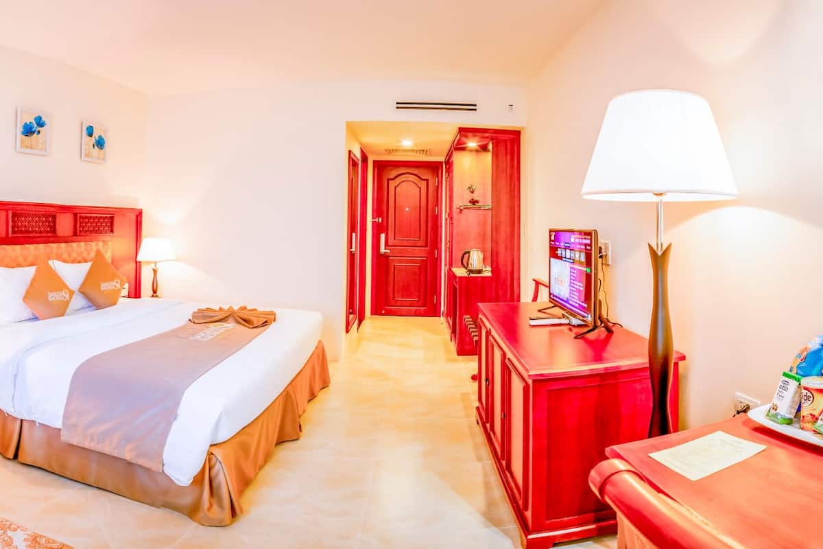 A hotel room with a bed, a chair, a desk, a TV, and a lamp.