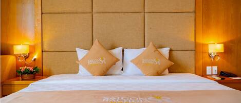 Una habitación de hotel con una cama grande, dos almohadas con el logotipo del hotel, lámparas de noche y una colcha a cuadros.