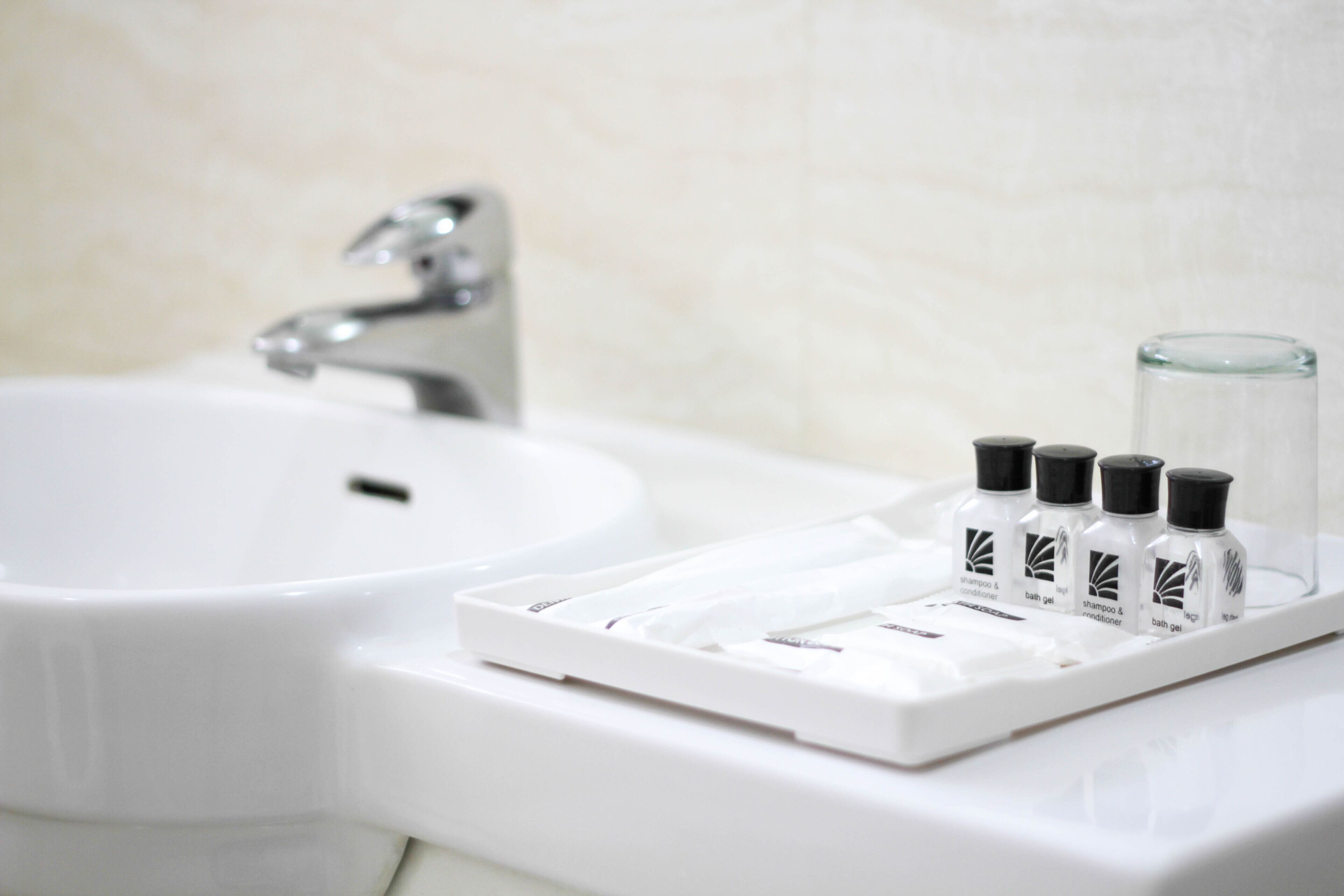 A bathroom sink with a glass of water and four bottles of shampoo and conditioner.