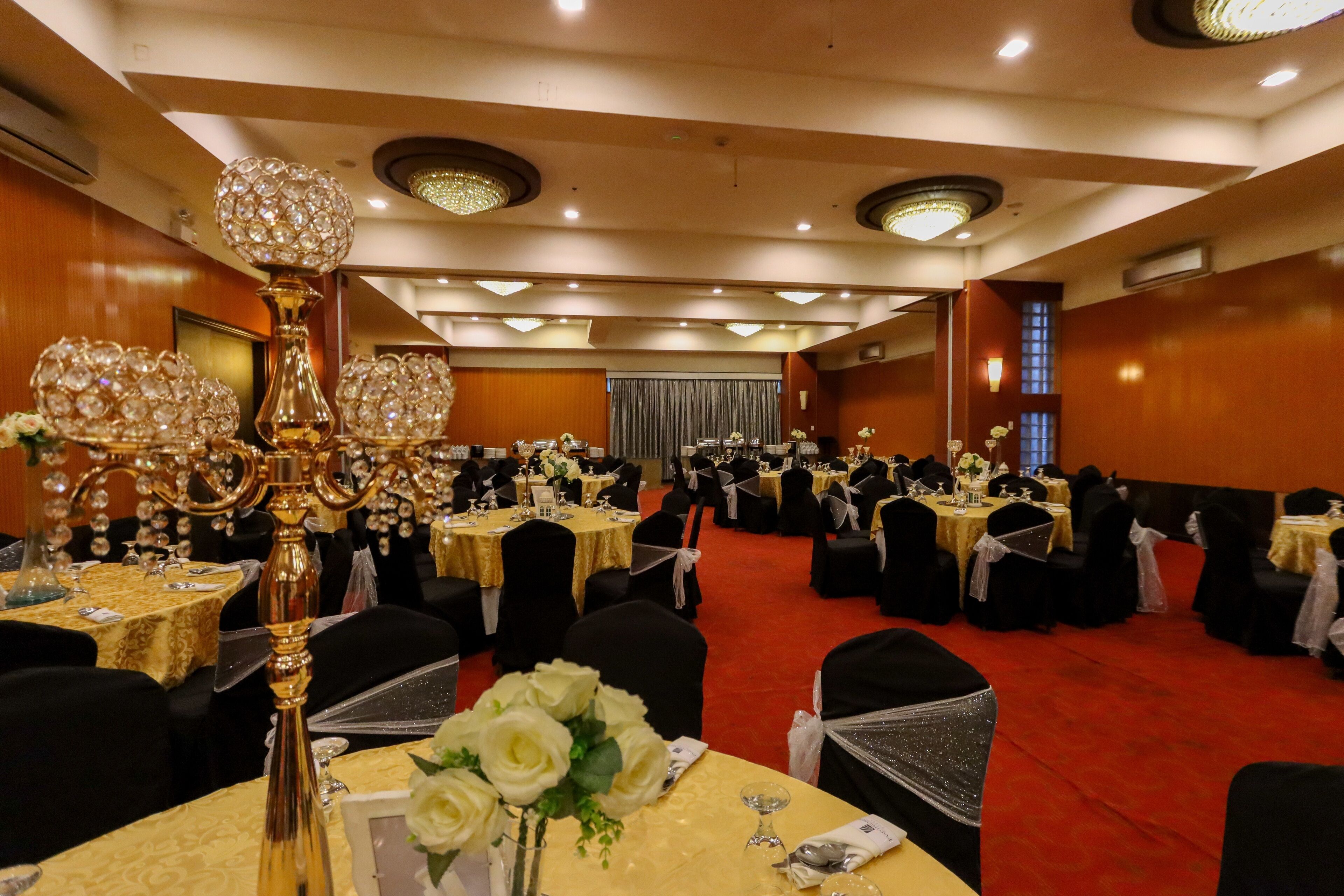 A banquet hall with round tables, black chairs, and chandeliers.