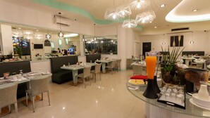 A modern restaurant with glass tables and booths, overhead lighting, and a buffet area with food and drinks. - Paseo Premiere Hotel (Santa Rosa)