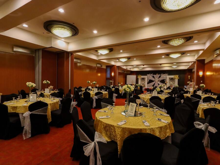 Un salón de banquetes con mesas redondas, sillas negras y manteles amarillos.