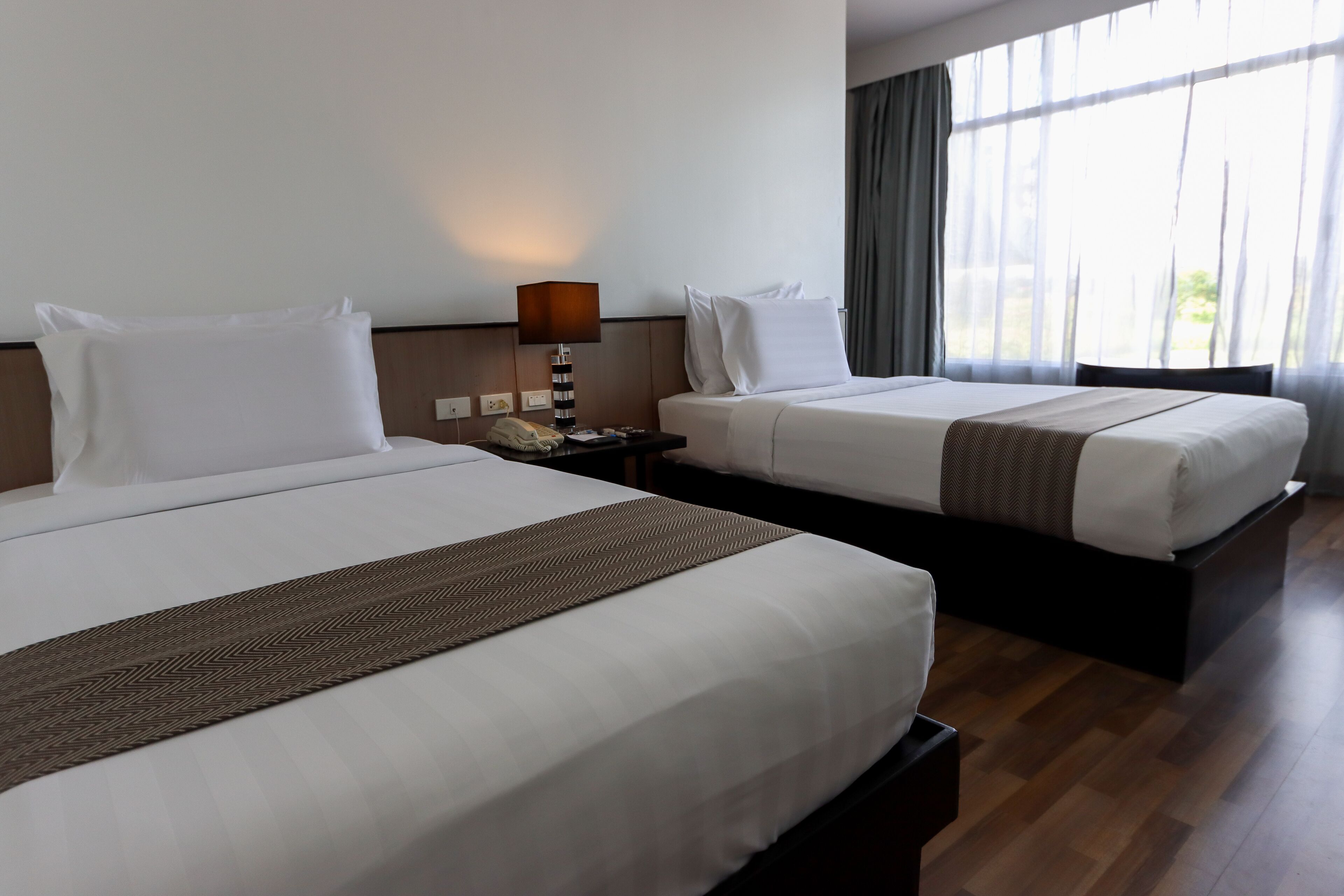 Une chambre d’hôtel avec deux lits, une table de chevet avec une lampe et une fenêtre avec des rideaux.