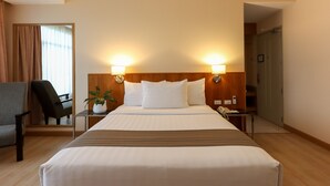 A hotel room with a large bed, two bedside lamps, a chair, a small table with a plant, and a phone on the nightstand. - Paseo Premiere Hotel (Santa Rosa)
