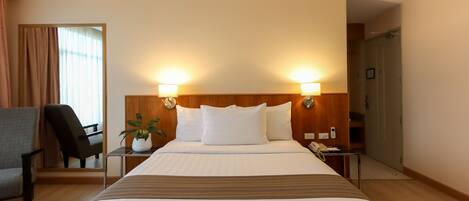A hotel room with a large bed, two bedside lamps, a chair, a small table with a plant, and a phone on the nightstand.