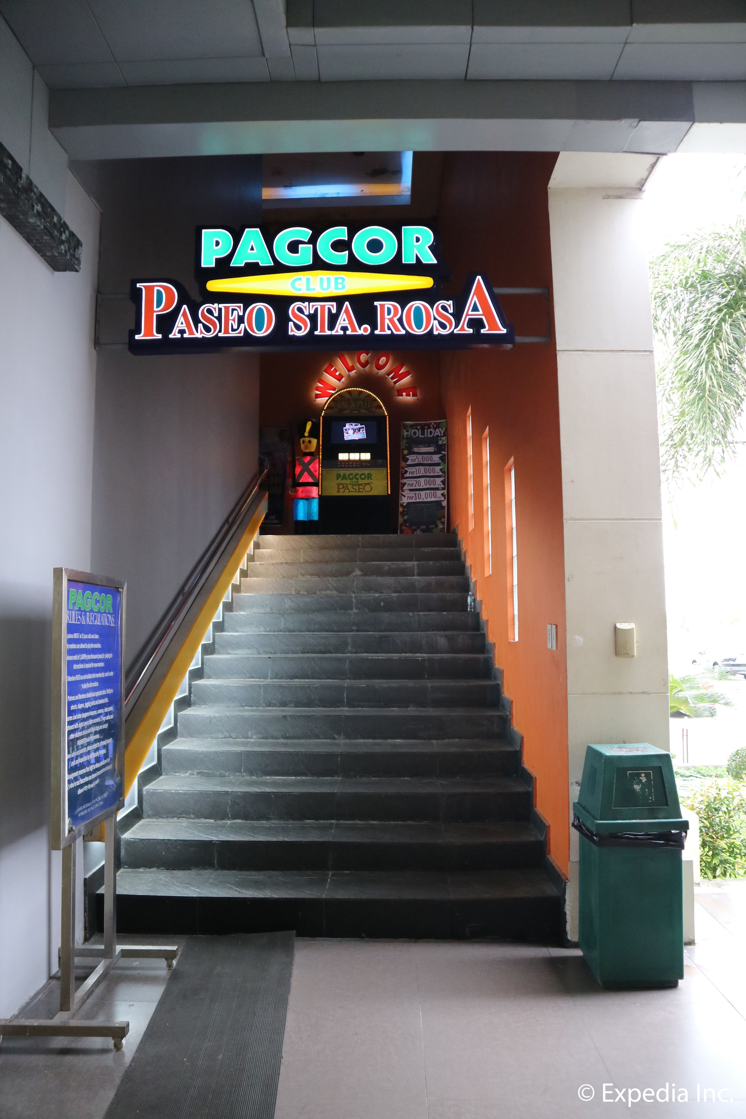 A staircase leading to a club entrance with a neon sign, a trash bin, and a signboard.