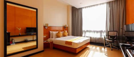 A hotel room with a large bed, a desk, a television, and a large mirror.