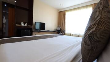 A hotel room with a large bed, a television, a desk with a computer, and a window with curtains.