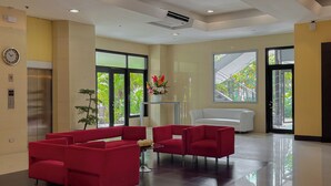 A modern lobby with red seating, a clock, an elevator, and large windows with a view of greenery. - Paseo Premiere Hotel (Santa Rosa)