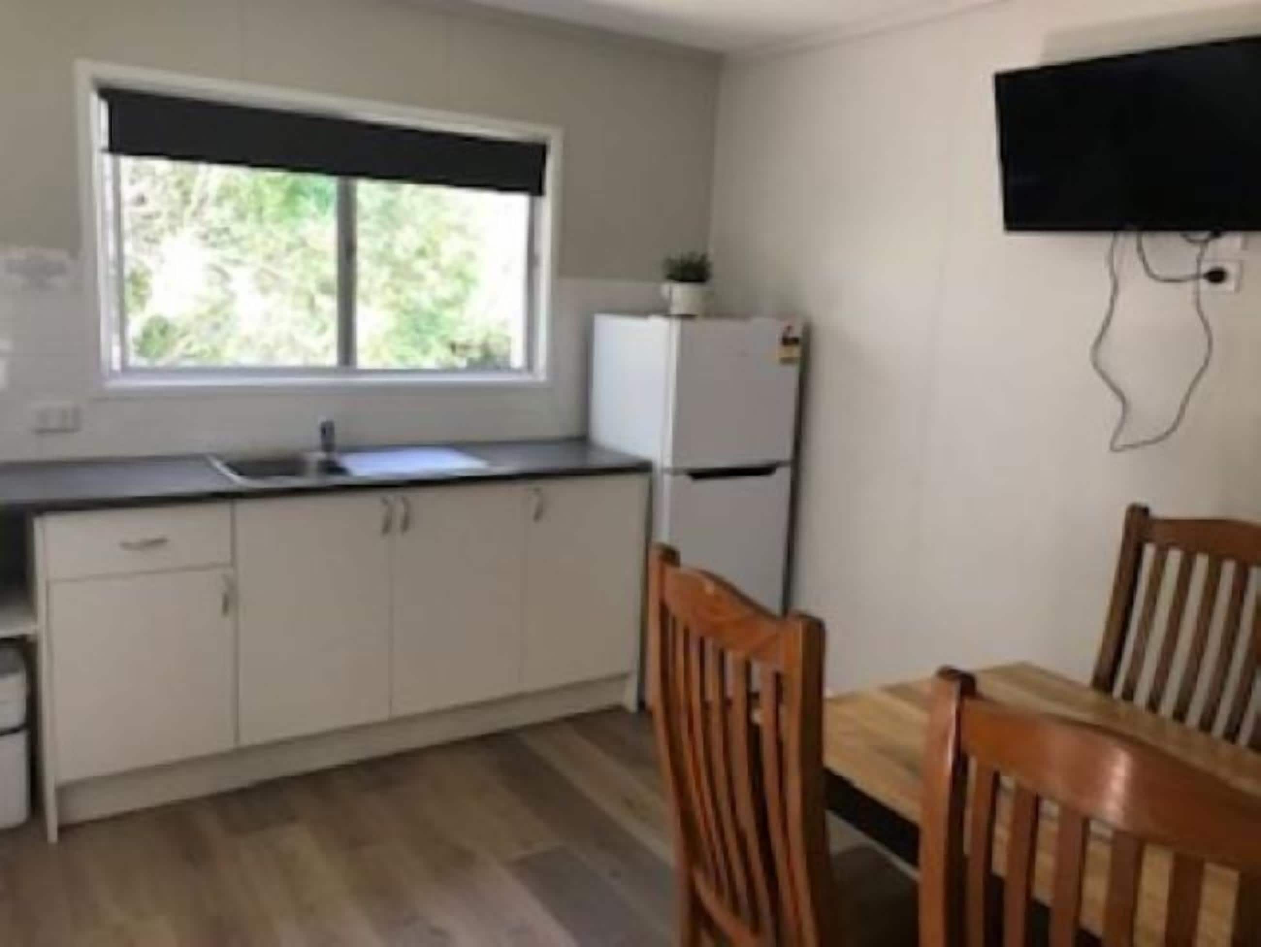 Una pequeña cocina con ventana, un refrigerador y una mesa de comedor con sillas.