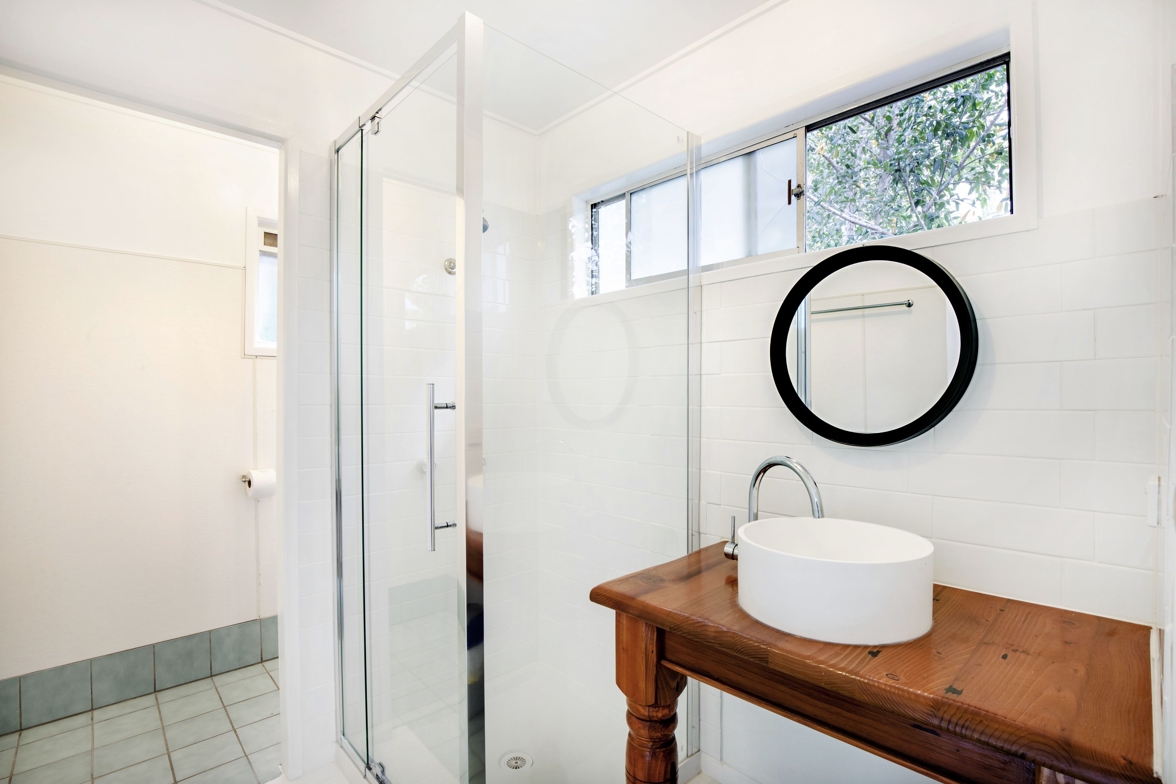 A bathroom with a glass shower door, a wooden vanity with a sink, and a window above the mirror.