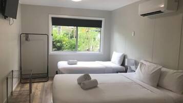 A hotel room with two beds, a TV, an air conditioner, and a window with a view of greenery.