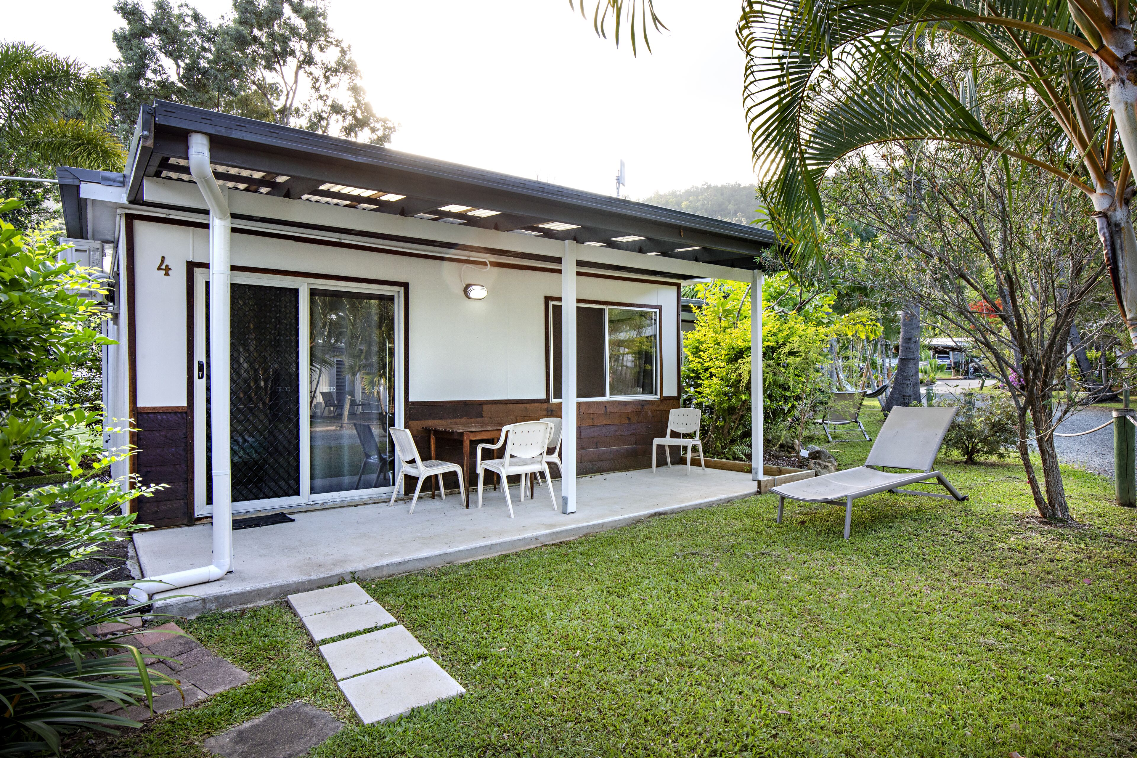 A modern house with a covered patio, a dining area with chairs, and a lawn.