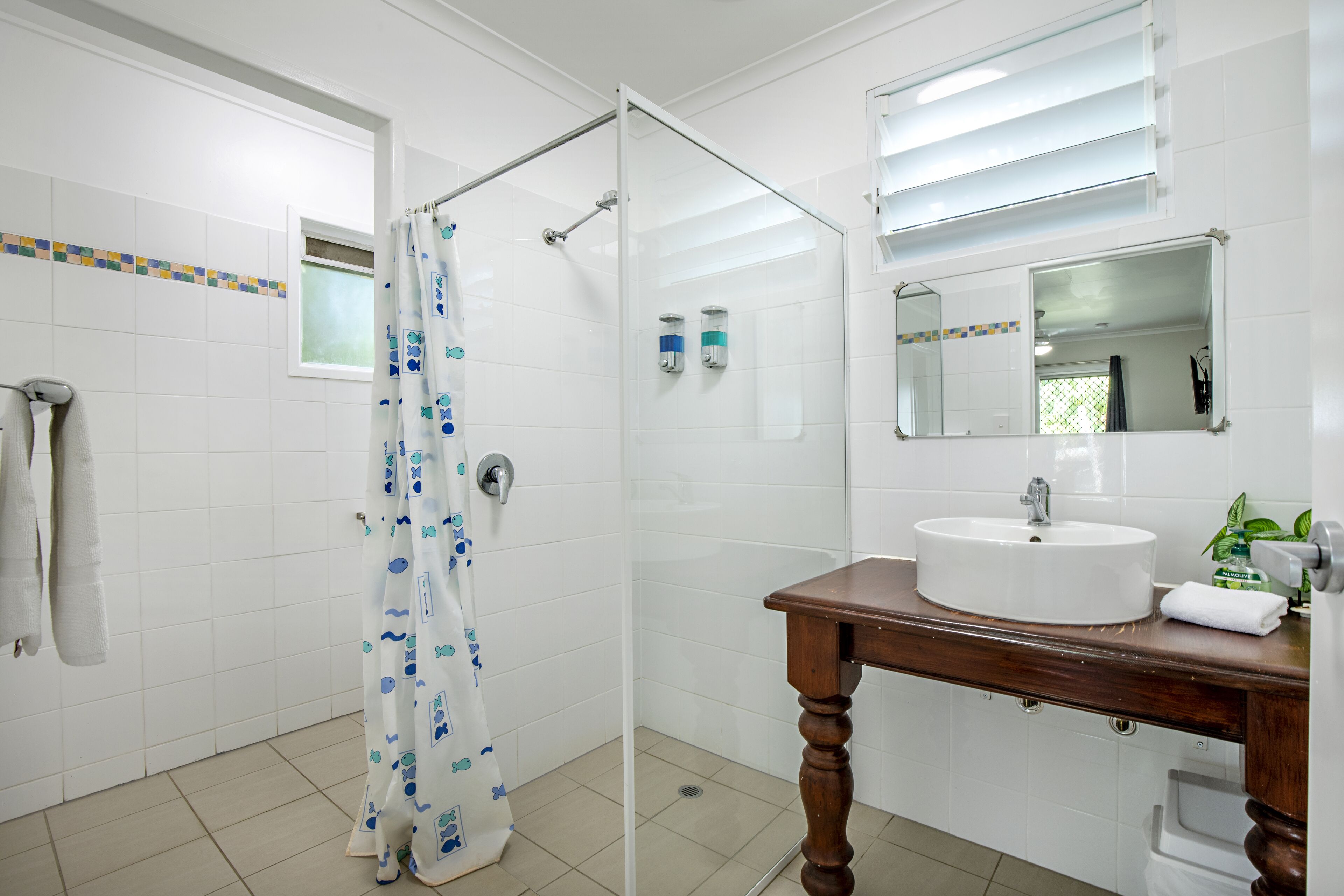 A bathroom with a glass shower enclosure, a white sink with a wooden vanity, and a mirror above the sink.
