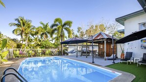 Uma piscina com escada de metal, rodeada por palmeiras e uma rede.
