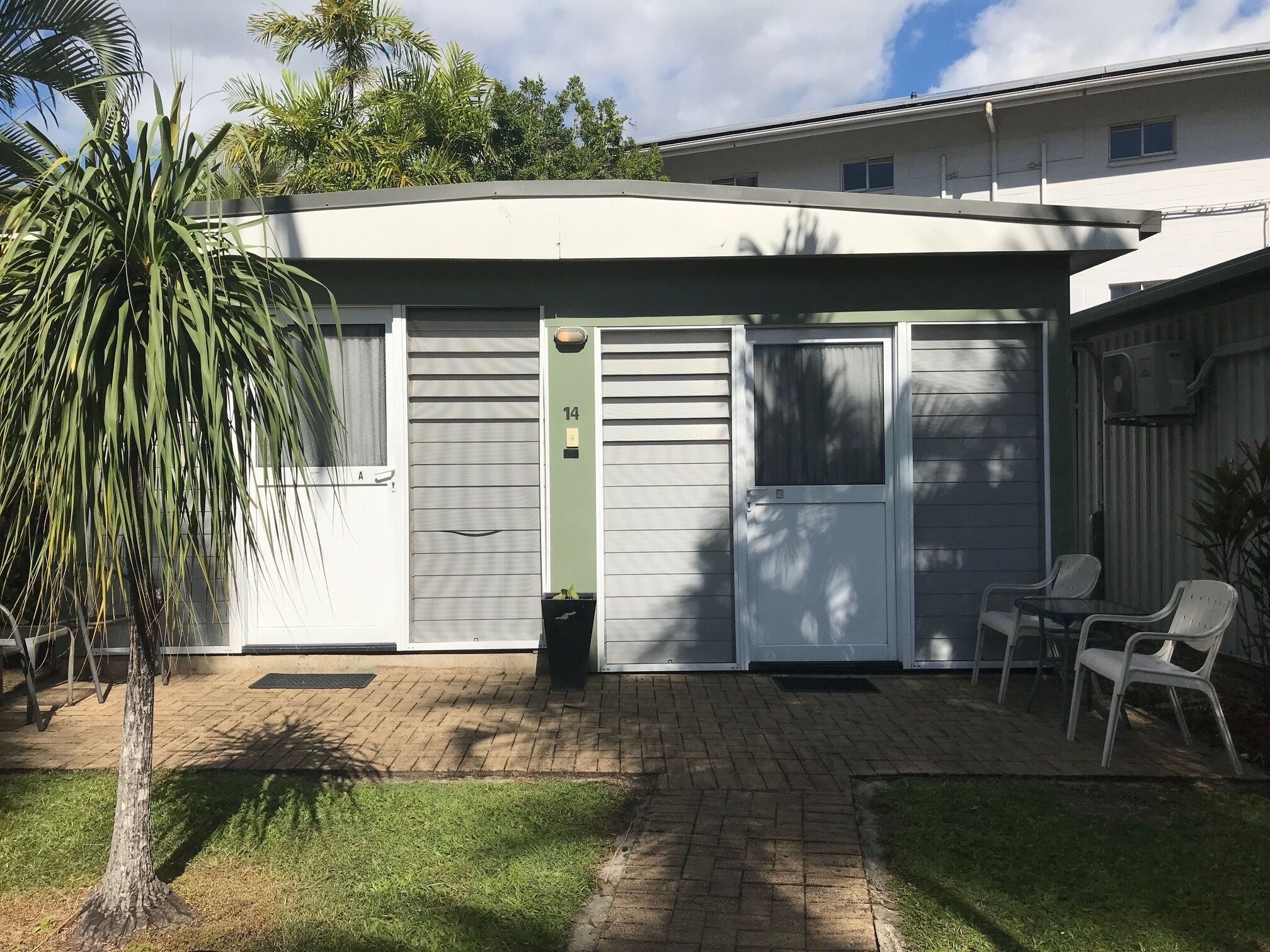 Un immeuble résidentiel doté d’un portail de garage, d’un petit espace extérieur aménagé avec deux chaises et d’un pot de fleurs.