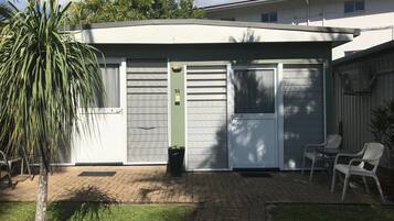 Un immeuble résidentiel doté d’un portail de garage, d’un petit espace extérieur aménagé avec deux chaises et d’un pot de fleurs.