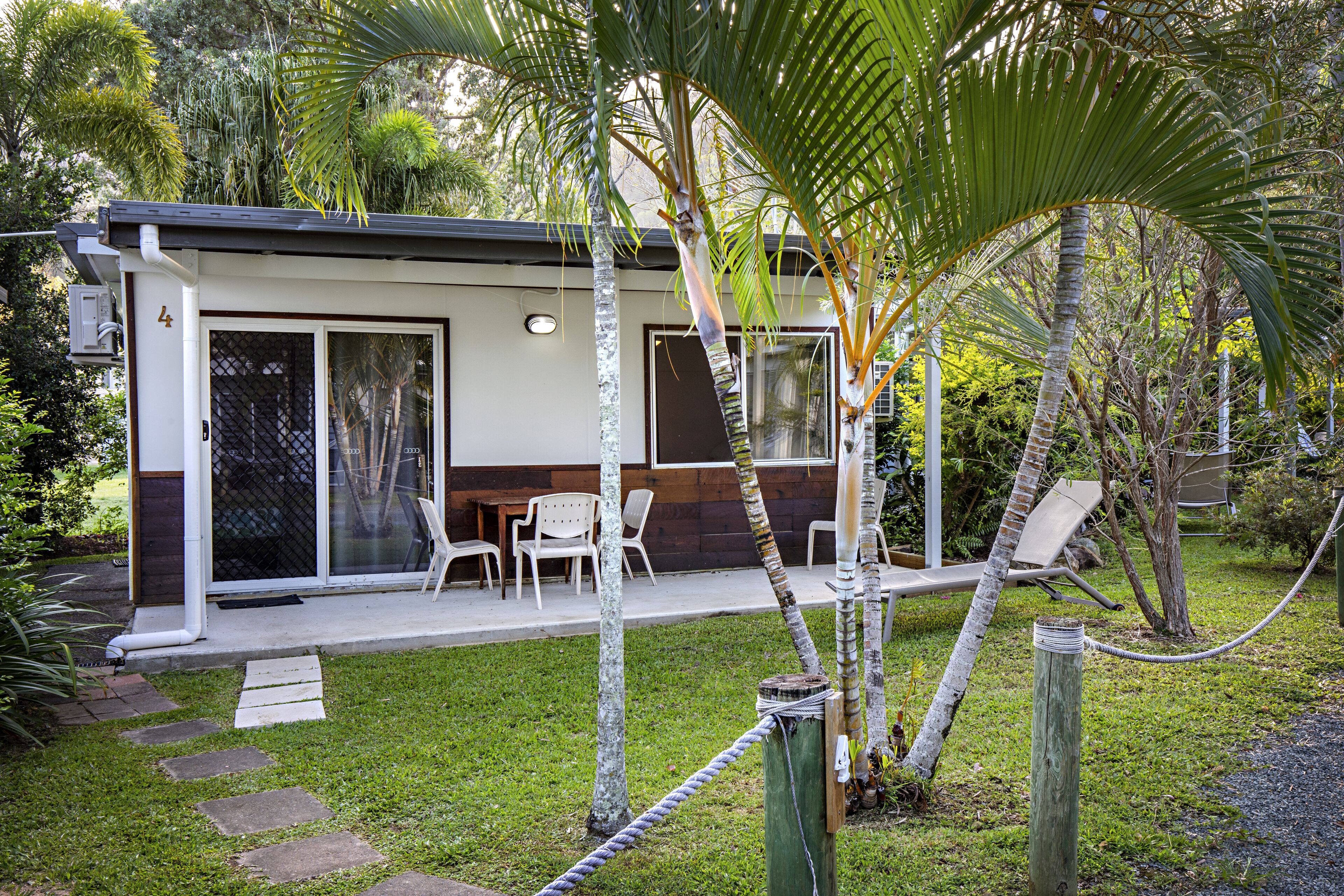 Una casa moderna con un porche cubierto, sillas blancas y una pequeña zona de piscina.