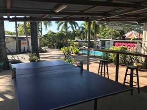 A covered outdoor area with a ping pong table, a pool, and a hammock. - Bush Village Holiday Cabins (Cannonvale)