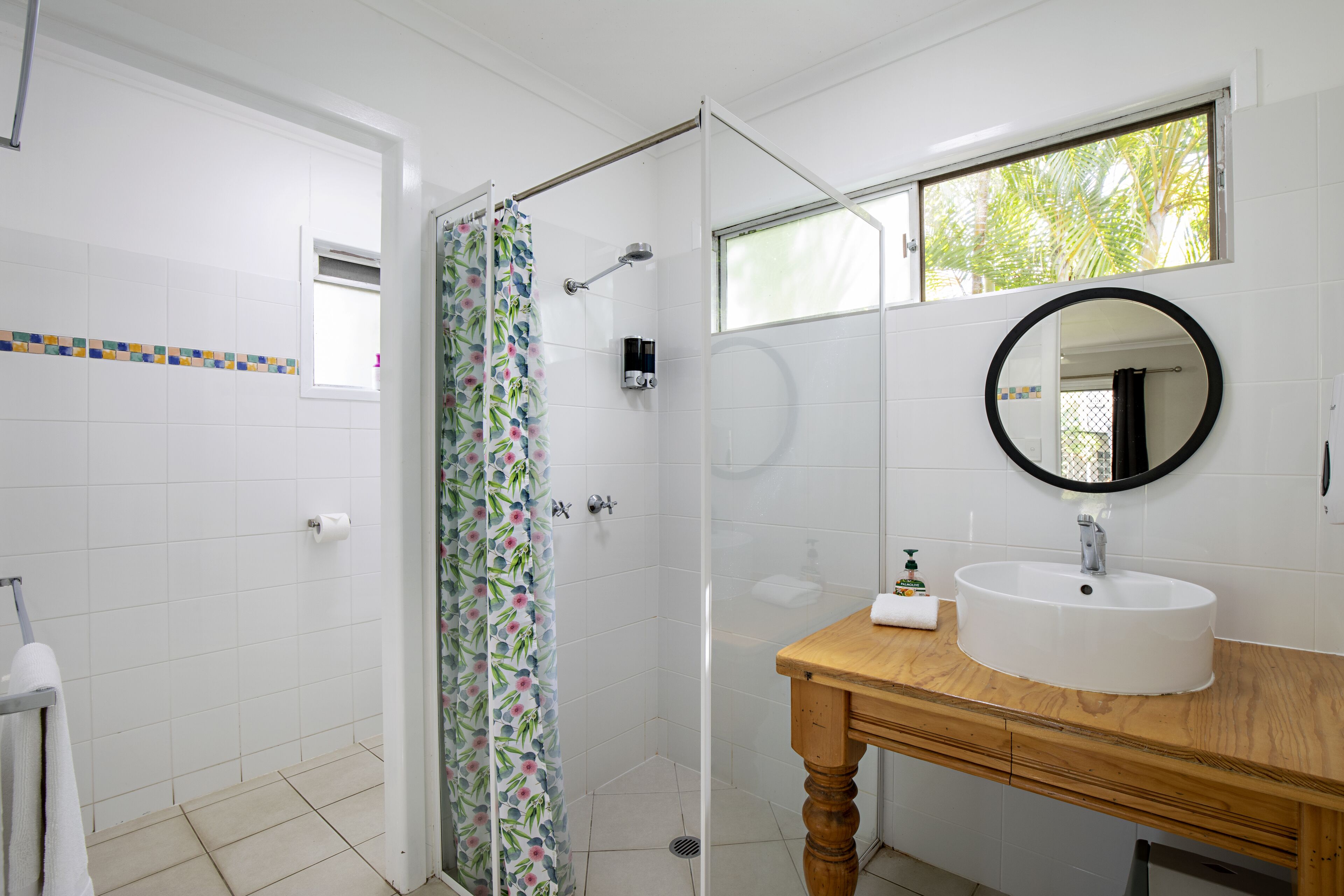 A bathroom with a shower, a sink, a mirror, and a window.