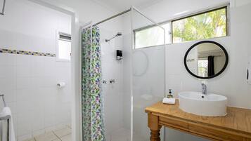 A bathroom with a shower, a sink, a mirror, and a window.