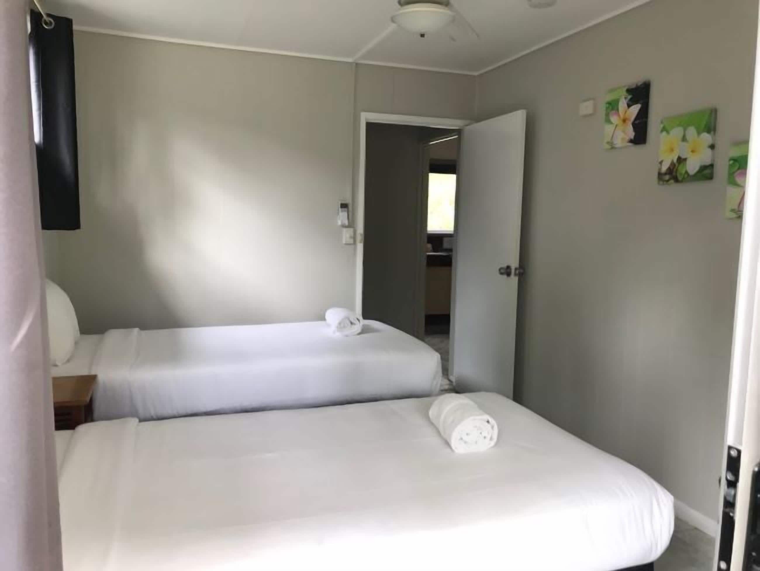 A hotel room with two single beds, a flat-screen TV, and a door leading to a bathroom.