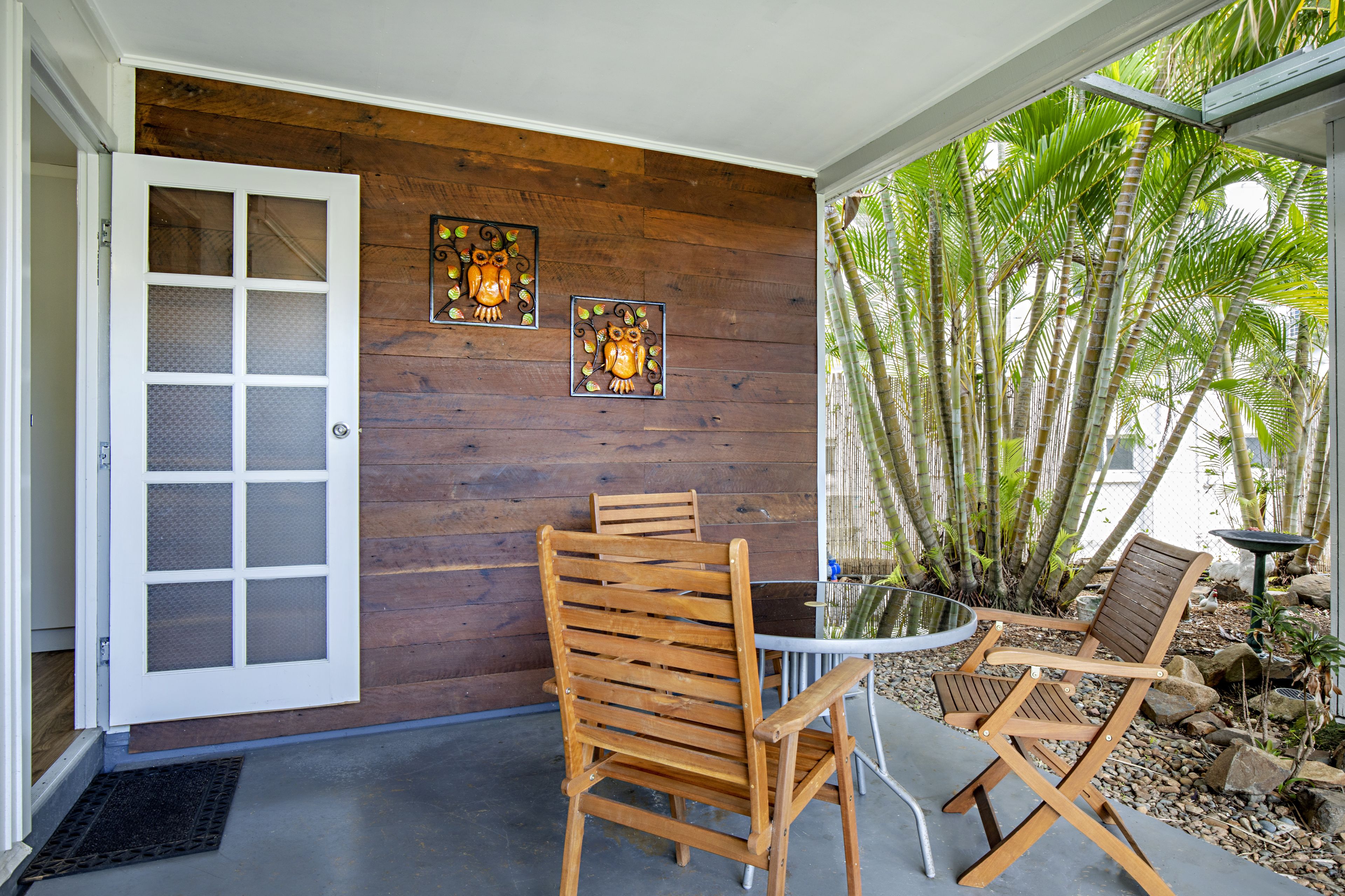 Un mur en bois orné de deux décorations représentant des hiboux, une porte en verre et un espace patio avec une table et des chaises.