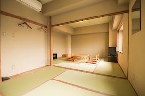 Una habitación japonesa tradicional con suelo de tatami, una mesa baja con cojines, un televisor y una percha para la ropa.