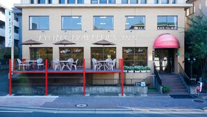 A hotel with a red exterior, multiple windows, and outdoor seating with umbrellas. - Kyoto Travelers Inn (Kyoto)